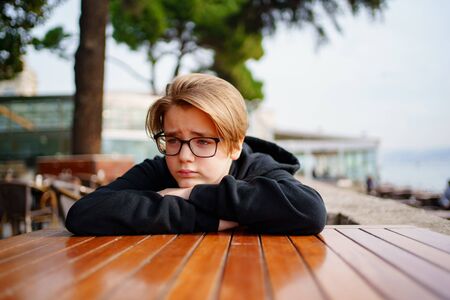 Teen blond with glasses dressed in black sitting at a table in the outdoor cafeの写真素材