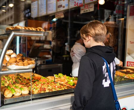 The teenager in black clothes standing at the counter with the street food, rear view