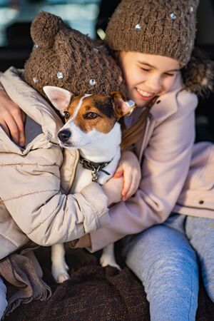 Two sisters in winter clothes sitting in the trunk of a car with dog and play. It is winter and snow.の写真素材