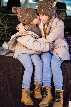 Two sisters sitting at the top in the trunk of a car and a hug. Outdoors in the winter.の写真素材