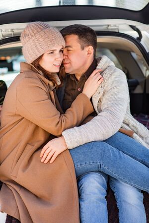 Man and woman sitting in the trunk of the white car in the winter around snowの写真素材