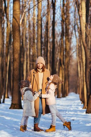 Mother and daughters in hats hugging in the winter snow forest. Face in the camera. Family and love.の写真素材