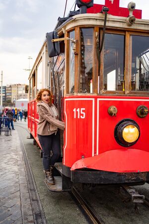 funny girl in a brown jacket is stand on the running Board of a redtram in the rainの写真素材