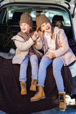 Two sisters sitting at the top in the trunk of a car and  pull the tail. Outdoors in the winter.の写真素材