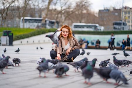 girl is sitting on a tile on the square and around the pigeons. Taksim Istanbulの写真素材
