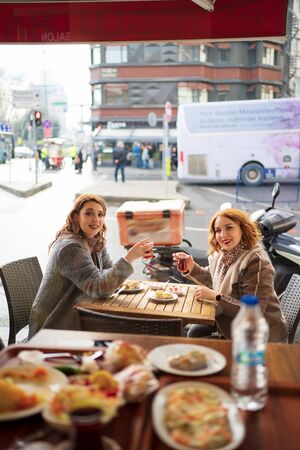 Two cheerful girlfriends sitting in cafe on the street and drink teaの写真素材