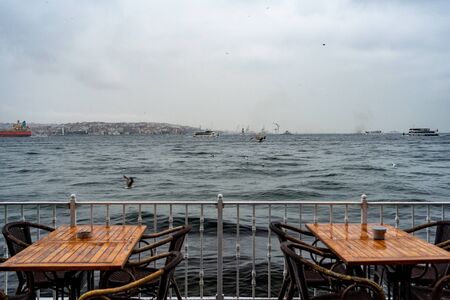 two tables at an outdoor cafe on the seafront in the cold season against the sea waves Seagull in the skyの写真素材