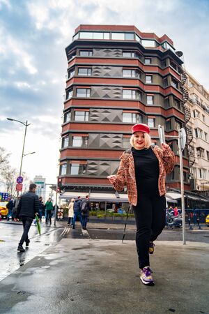a blonde girl in a cap stands on the street against the background of the road and buildingsの写真素材