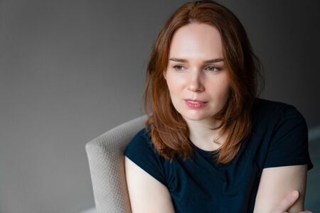 A girl with brown hair in a black t-shirt sits and looks awayの写真素材