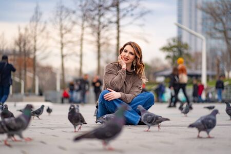 girl is sitting on a tile on the square and around the pigeons. Taksim Istanbulの写真素材