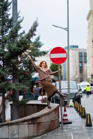 a cheerful red-haired girl stands by the road and holds on to a road signの写真素材
