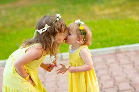 Two sisters in flower wreaths and yellow dresses kiss in a hotel Park in Turkey. Walking in the fresh air in summer.の写真素材