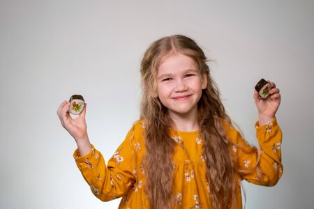 A little girl holds rolls in her hands. Japanese cuisine with home delivery. On a white background in an orange dress. Long curly hair.の写真素材