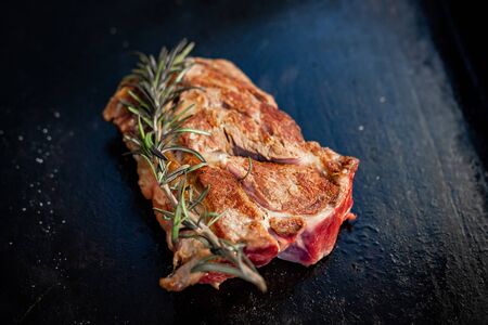 large fried piece of meat on a hot plate with rosemary. Cooking in the kitchen at the restaurant. A...