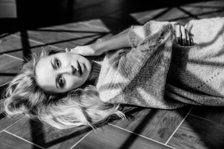a Beautiful slim blonde girl lies on the floor by the window and touches her hair. Sunlight. Black and white.の写真素材