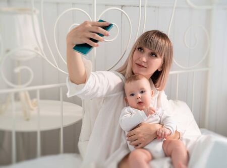 close up. mom with long blonde hair lying in bed with the baby and taking a selfie on your...