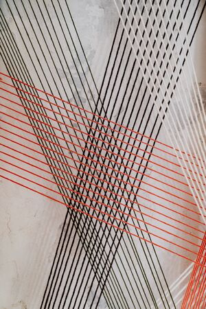 black, white and red threads on a background of textured plaster on the wall