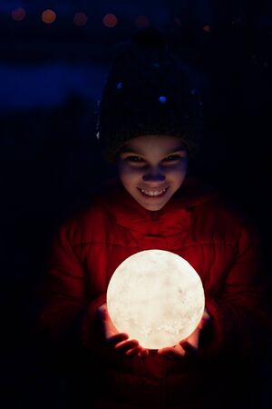 teenager girl in a cap and a red jacket holds a full glowing moon