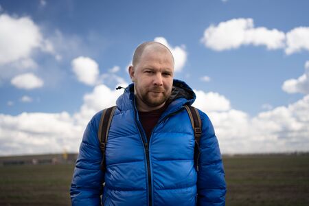 a man in a medical mask and a blue jacket stands in a field on the background of the runway of the...