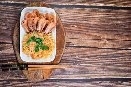 Udon noodles and fried cocktail prawns on a white plate. wooden Board on the background. copy space.の写真素材