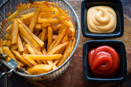 potatoes fries in the basket from the fryer and sauces red and white. close-up. wooden Board.