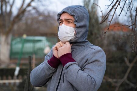 profile man in a gray jacket with a hood in the medical protective mask on the street during an epidemic of pneumonia.の写真素材