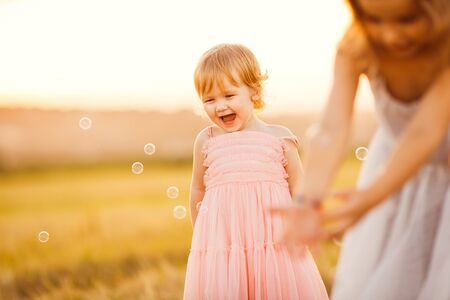 kid girl chasing soap bubbles on the sloping wheat field at sunset in villageの写真素材