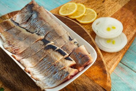 sliced salted fish herring on a plate on wooden Board with herbs, with onion rings and lemon. close up.の写真素材
