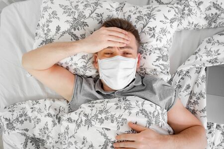 the masked male lies at home in bed and sick. stay home for the quarantine period.の写真素材