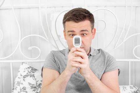 close up. man freelancer is sick, measures the temperature and working from home in the bedroom at...