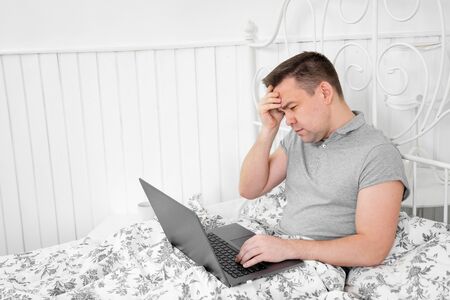 small business. male freelancer is sick and working from home in the bedroom at the computer during...
