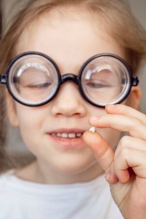 funny little blonde girl with glasses with the fallen milk tooth in his hand. dental care. tooth...