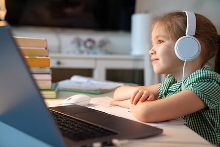 kid with blond hair in a green dress in headphones listens to music, online lesson on the laptop....