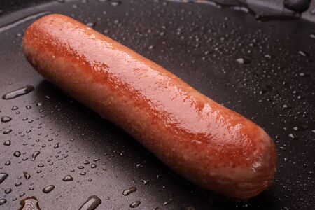 one sausage fried in a pan with drops of oil. fat quick breakfast at home.の写真素材