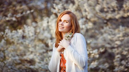 woman with red hair standing in a flowering bush with bouquet branches of flowers in their hands. warm spring and blossom.の写真素材
