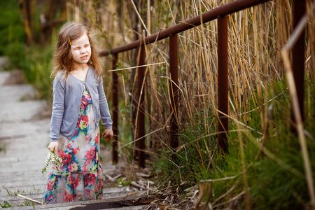 a little girl close eyes, standing on the stairs with a high handrail along the dry tussocks.