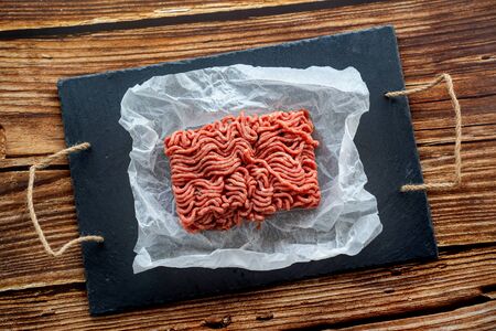 the minced meat on the cooking paper and stone tray on a wooden table. prefabricated patties.