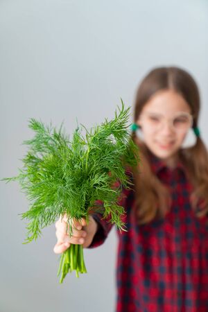 Cute teen schoolgirl showing fresh herbs like dill edible bunch of flowers over white background, concept hairstyle edible, healthy food, vegetarianism and the raw food diet.の写真素材