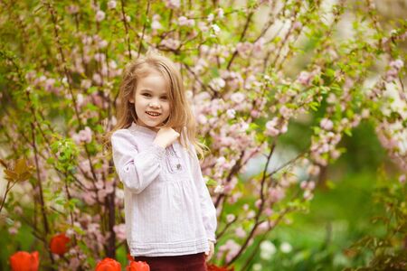 funny girl with blond long hair near flowering pink almond bush and tulips. the spring bloom.の写真素材