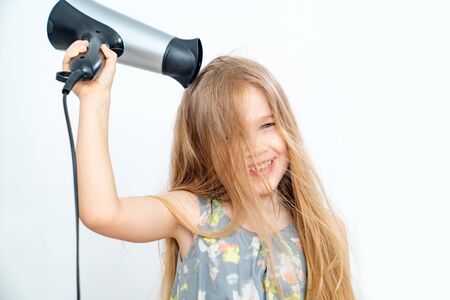 Cute smiling little child girl drying her long hair with hair dryer. independent children. hair care.の写真素材