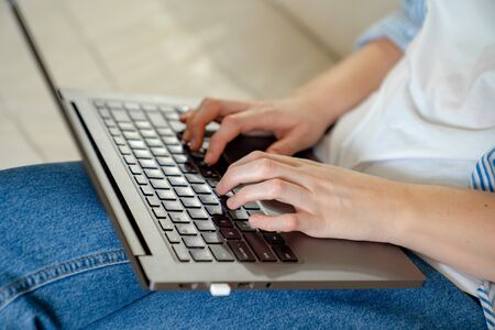 close up. hands. woman on laptop typing text checking email online sitting on sofa, searching for...