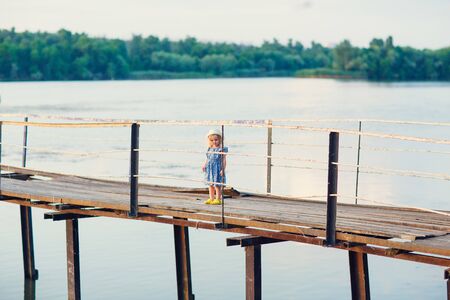 in the summer the kid girl in blue clothes standing on the old bridge broken bridge on the background river. Pier on the river, naval station.の写真素材