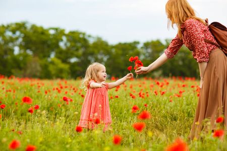 Beautiful little child girl in dress with mom picking flowers in poppy field.の写真素材