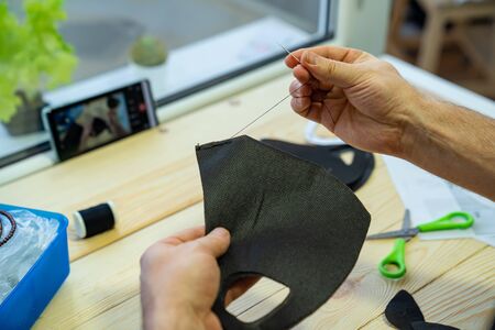 mens hands sew with a needle. fabrics and sewing accessories for sewing an anti-virus mask. Zero waste and quarantine concept. Homemade black facemask against virus infection.の写真素材