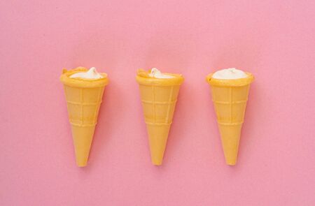 Vanilla cream in wafer cup. Vanilla ice cream cone on pink color background. Candy bar and cake...