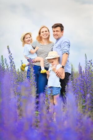 dad mom and daughters beautiful little kids girls in a field with tall blue purple flowers, summer landscape.の写真素材