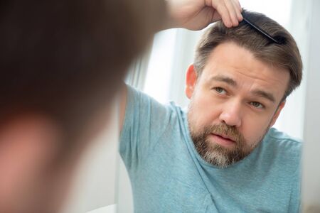 man in t-shirt combs comb your hair and beard looking in the mirror. the care and hygiene of the...