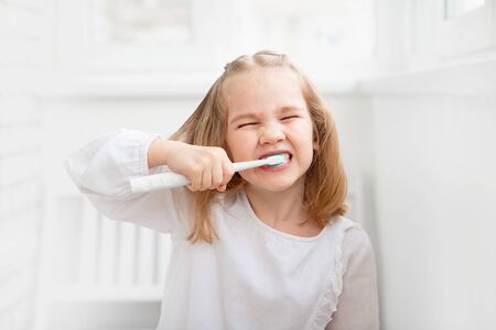 funny kid girl in the morning cleans the teeth electric toothbrush. The concept of daily care and hygiene of the oral cavity. prevention of dental caries.の写真素材