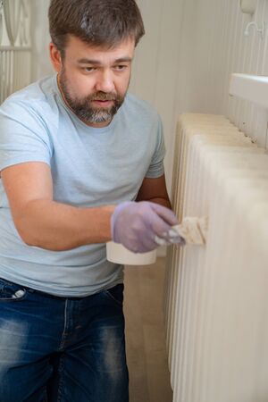 man in a glove painting a heating radiator with a paint roller in home. A DIY repair. Professional Workman Hand holding Dirty Paintbrush.の写真素材