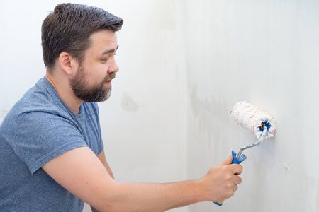 man painting roller wall with white paint. construction and repair work at home.の写真素材